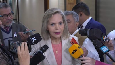 Lilian Samaniego en blazer claro y blusa roja, rodeada de periodistas que la entrevistan en un ambiente institucional.