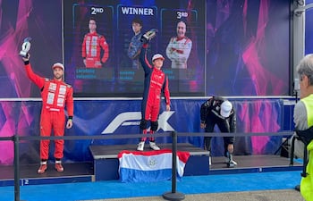 Mateo Valente en traje rojo sostiene un trofeo, sonriente. Valentino Carofano y Felisa Blanco lo acompañan en el podio con expresiones variadas.