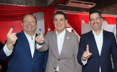 Horacio Cartes con blazer oscuro, Camilo Pérez en suéter gris, y Raúl Latorre en chaqueta azul, todos sonriendo y mostrando sus dedos con tinta.