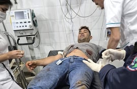 Hombre tendido en camilla con herida en el abdomen, rodeado de personal médico en un ambiente clínico.