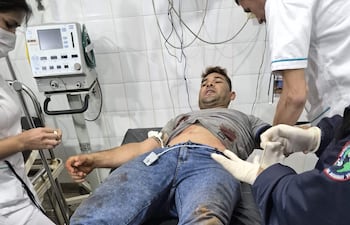 Hombre tendido en camilla con herida en el abdomen, rodeado de personal médico en un ambiente clínico.