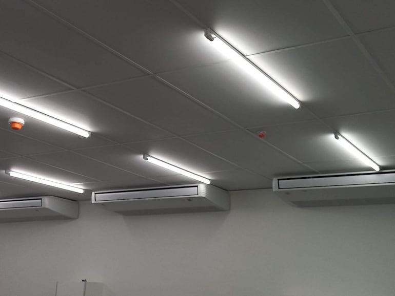 Techo de albergue renovado con luces fluorescentes y unidades de aire acondicionado visibles.