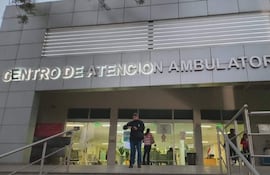Hombre de pie revisando su reloj en el Centro de Atención Ambulatoria (CAA) del IPS, dos personas al fondo en ambiente exterior con escaleras.