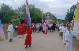 Tres figuras con túnicas religiosas, una en manto rojo, marchan con estandarte en celebración, con un entorno residencial y árboles.