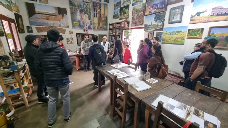 Grupo de personas, incluyendo un guía de pie, discutiendo rodeados de obras de arte en un ambiente acogedor.