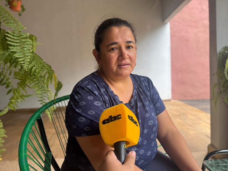 Mujer con blusa floral oscura y expresión seria, sentada en un ambiente interior, mientras un micrófono se acerca a ella.