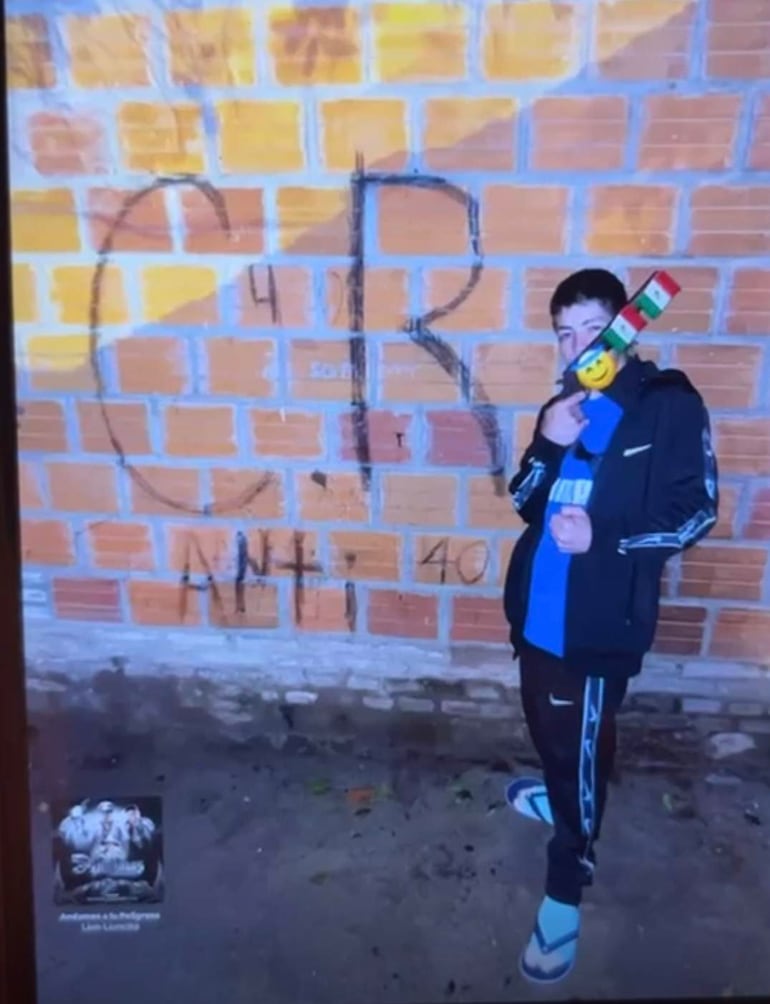Joven de pie frente a pared amarilla, sosteniendo un juguete que simula ser un arma, con inscripciones visibles en la pared.