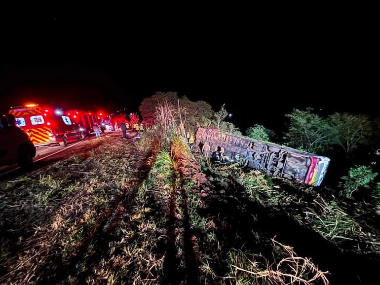 Autobús volcado en el centro de la escena, rodeado de ambulancias y rescatistas en la oscuridad de la noche.