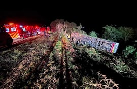Autobús volcado en el centro de la escena, rodeado de ambulancias y rescatistas en la oscuridad de la noche.