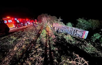 Autobús volcado en el centro de la escena, rodeado de ambulancias y rescatistas en la oscuridad de la noche.