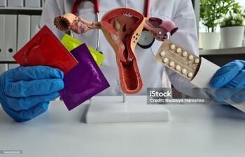 Una médica con guantes de látex sostiene preservativos, condones, pastillas anticonceptivas y muestra un útero de plástico