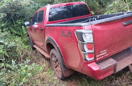 Camioneta Isuzu D-Max roja atrapada en vegetación densa, cubierta de barro, en un entorno rural sin personas visibles.