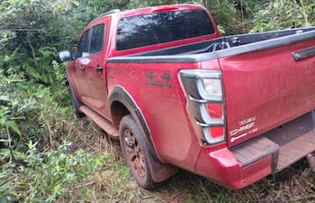 Camioneta Isuzu D-Max roja atrapada en vegetación densa, cubierta de barro, en un entorno rural sin personas visibles.