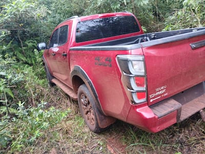 Camioneta Isuzu D-Max roja atrapada en vegetación densa, cubierta de barro, en un entorno rural sin personas visibles.
