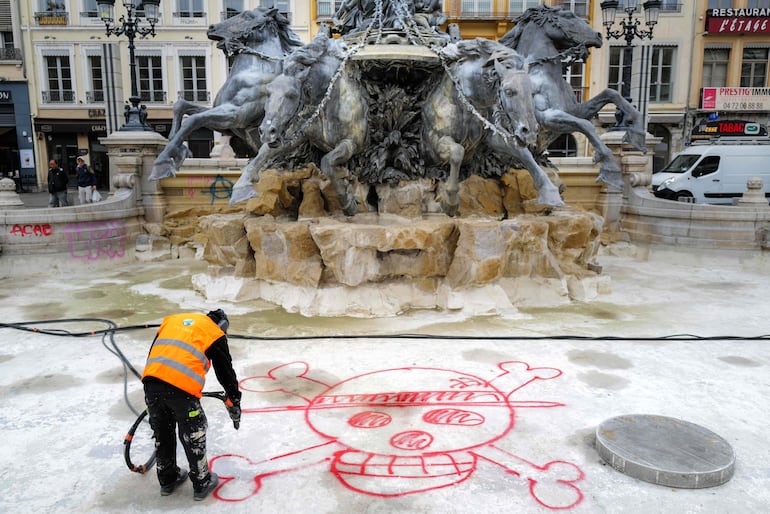 Un empleado municipal retira una pintada de la fuente Bartholdi en la plaza des Terreaux, en Lyon, dos días después de que se produjeran disturbios y saqueos al margen de las manifestaciones a escala nacional contra el costo de la vida.