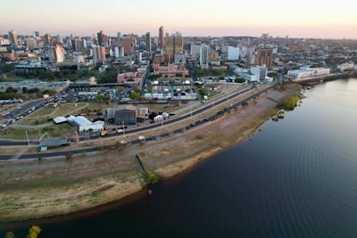 Vista aérea de Asunción al atardecer, con edificios destacando y el río visible en el primer plano.