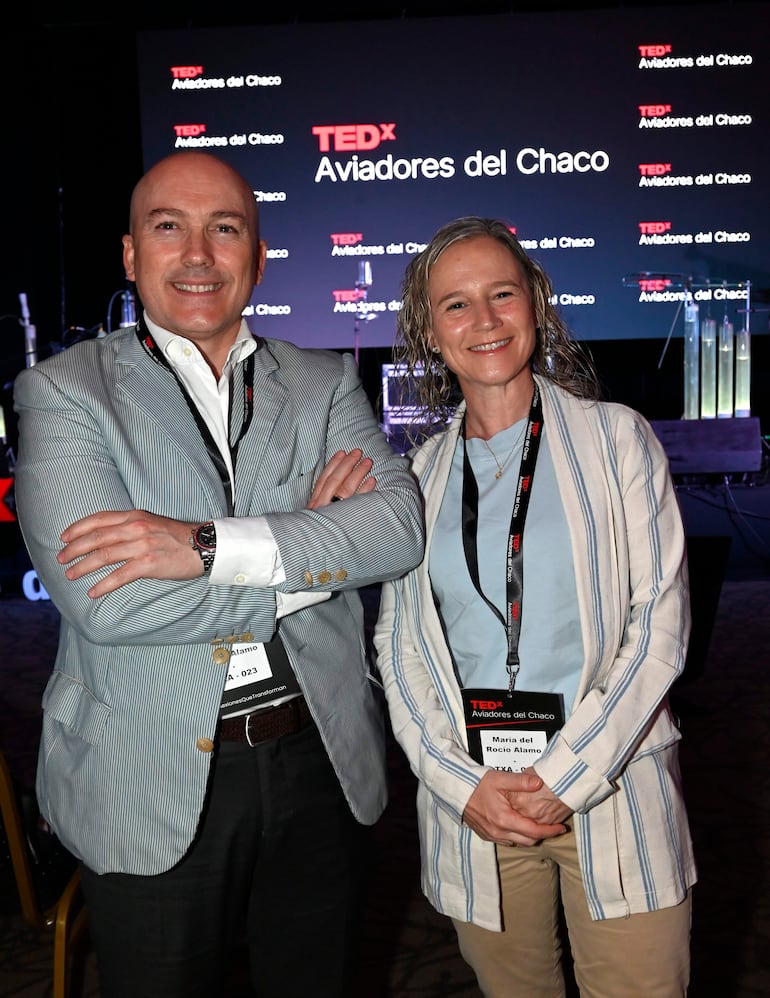 Hombre con camisa a rayas y blazer claro junto a mujer con abrigo a rayas y blusa azul, ambos sonríen en el evento TEDx.