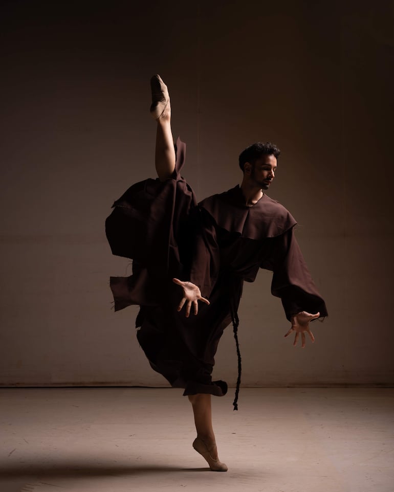 Bailarín en traje marrón en pose dinámica, con fondo oscuro que resalta su figura, en un estudio de danza.