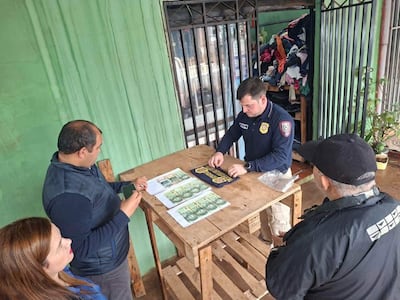 Hombre policía en camiseta, revisando documentos con billetes, acompañado por dos personas en un entorno informal.