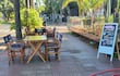 Escena de un café con mesas amarillas y un cartel de pizarra destacando desayunos y meriendas en un entorno tranquilo.