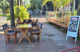 Escena de un café con mesas amarillas y un cartel de pizarra destacando desayunos y meriendas en un entorno tranquilo.