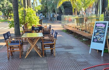 Escena de un café con mesas amarillas y un cartel de pizarra destacando desayunos y meriendas en un entorno tranquilo.