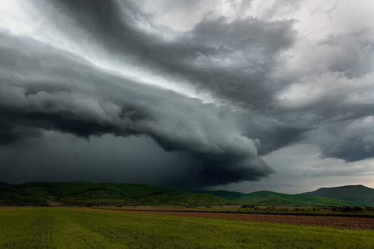 Cielo oscuro con cúmulos de nubes amenazantes sobre un campo verde en un entorno rural.