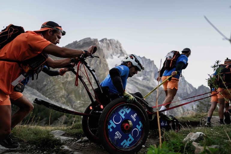 Un corredor de montaña en silla de ruedas es asistido por un grupo en el Arete du Mont Favre en la 23 edición del Ultra Trail du Mont Blanc (UTMB).