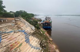 Barco azul atracado en un muelle deteriorado junto al río Paraguay en un ambiente natural y nublado.