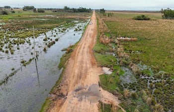 Paisaje rural con carretera de tierra y campos inundados, bajo un cielo gris, sin personas visibles.