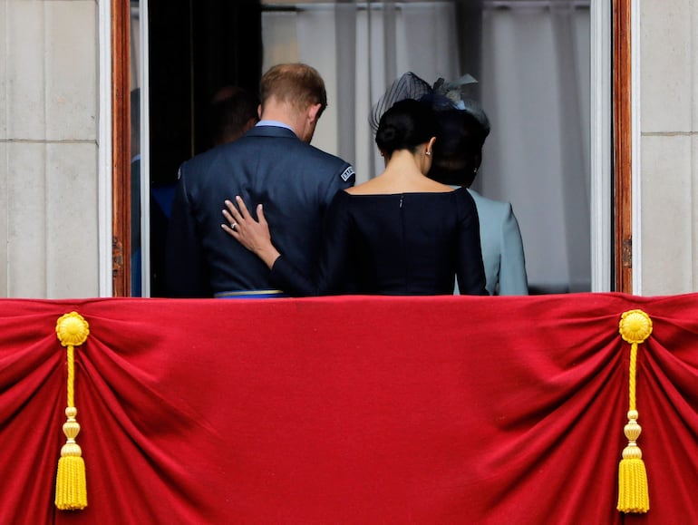 (FILES) Meghan, duquesa de Sussex (derecha), pone su mano en la espalda del príncipe Harry, duque de Sussex, mientras abandonan el balcón del Palacio de Buckingham el 10 de julio de 2018 tras presenciar un desfile aéreo militar para conmemorar el centenario de la Real Fuerza Aérea (RAF). Seis años después de renunciar a sus funciones como miembros de la realeza, el príncipe Harry y su esposa Meghan regresarán al Reino Unido en las próximas semanas. (Photo by Tolga AKMEN / AFP)