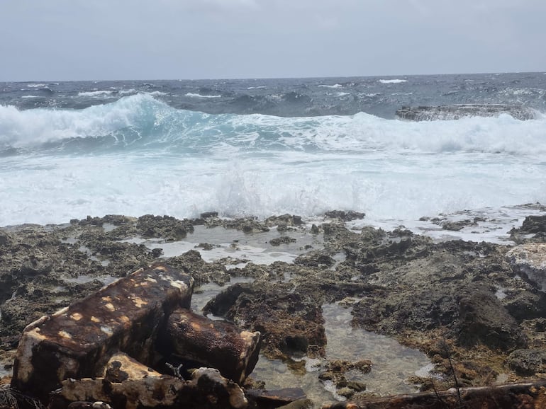 Faro gris con detalles rojos rodeado de un paisaje árido y cielo nublado, sin personas visibles.