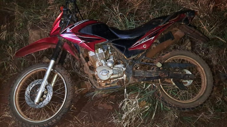 Motocicleta roja posicionada sobre terreno irregular con hierba y barro, sin personas presentes.