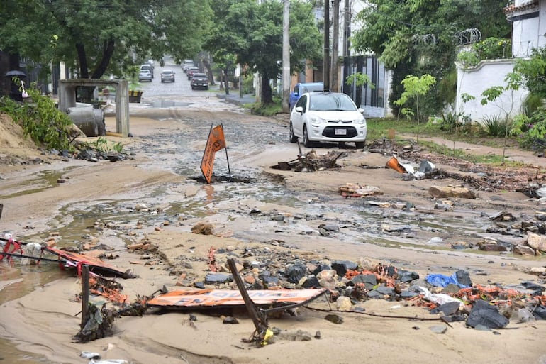 Escena de calle inundada con escombros y un vehículo blanco estacionado, sin personas presentes.