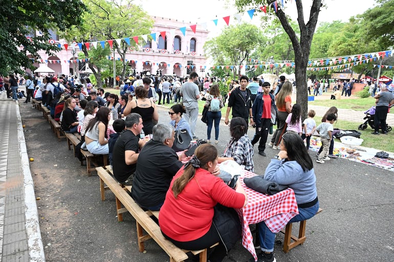 Asistentes a la fiesta visten ropa casual y disfrutan de una comida al aire libre, con decoración en colores patrios.