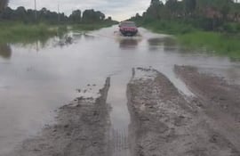 Vehículo todoterreno rojo avanzando por carretera inundada, rodeado de vegetación y cielo nublado.
