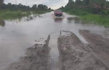 Vehículo todoterreno rojo avanzando por carretera inundada, rodeado de vegetación y cielo nublado.
