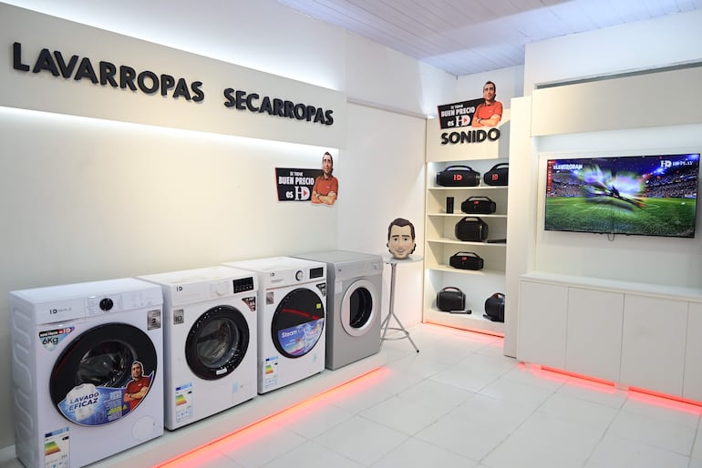 Local comercial exhibe lavarropas y secarropas de la marca HD, con carteles de precios y un televisor mostrando un campo de fútbol.