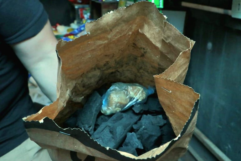 Saco de papel con carbón y un objeto envuelto en plástico en un entorno de almacén.