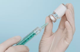 Manos con guantes sostienen una jeringa y un frasco de vidrio de una droga.