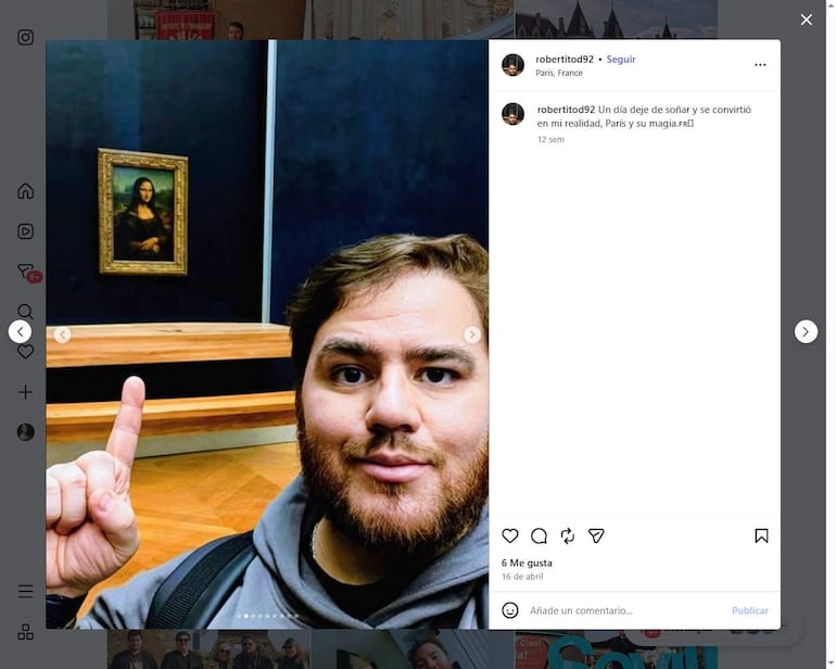 Roberto Moreno sonríe, señalando La Gioconda, vestido con chaqueta oscura en el Louvre, con un fondo oscuro y un banco de madera.