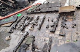 Varios rifles y armas dispersas sobre piso húmedo en un entorno caótico.