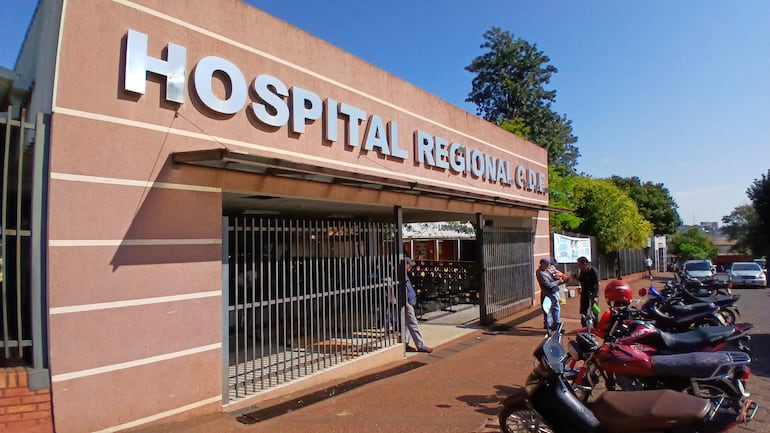 Fachada del Hospital Regional de Ciudad del Este con letrero grande. Dos personas interactuando al margen derecho.