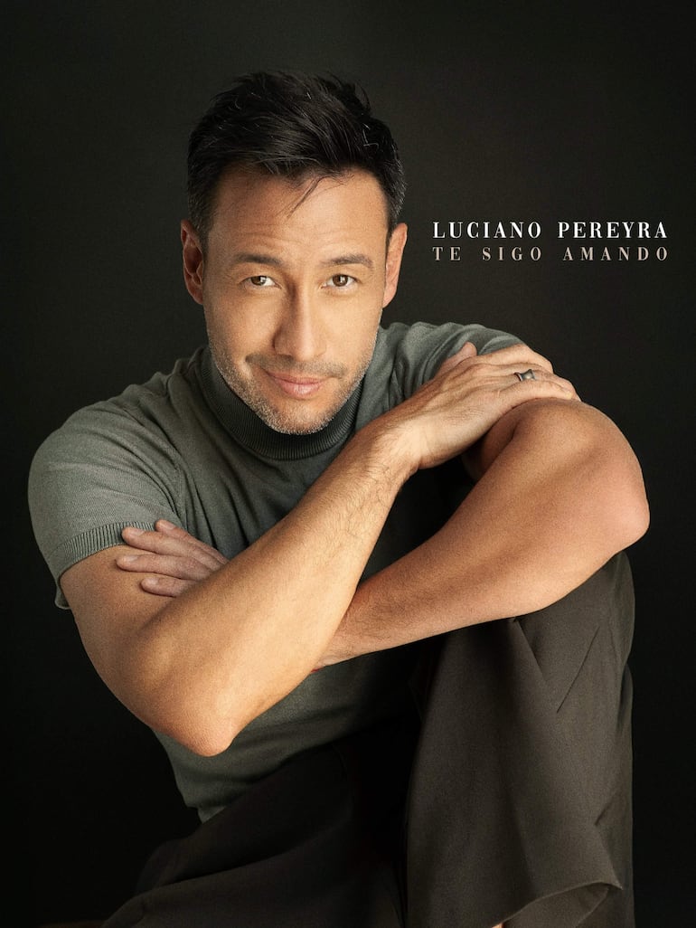 Luciano Pereyra sonríe en primer plano, con camiseta gris y fondo negro, durante una sesión fotográfica.