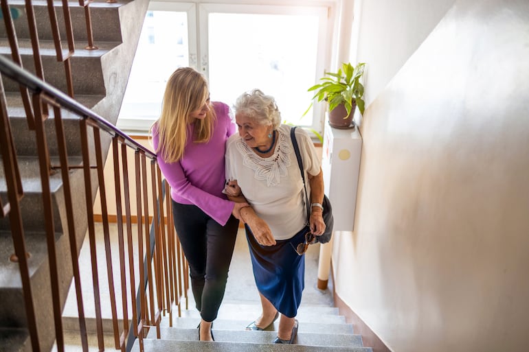 Una mujer ayuda a una persona mayor a subir las escaleras.