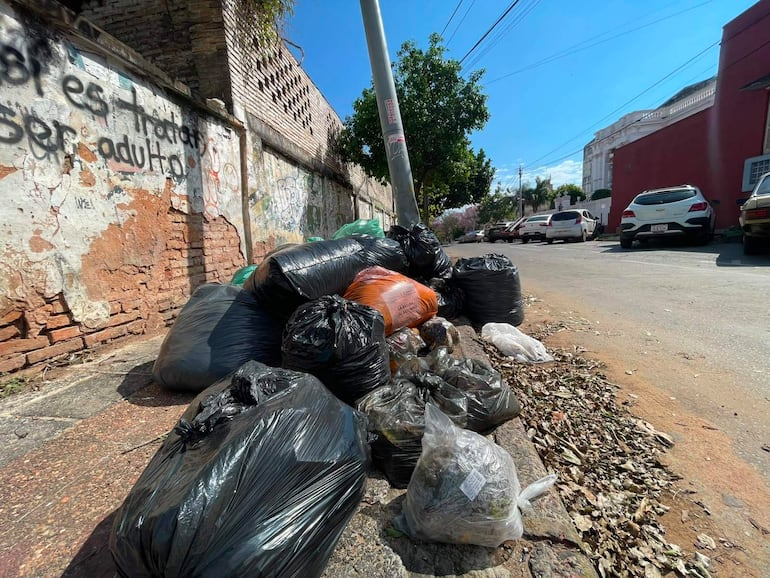 Montones de bolsas de basura en vereda de Asunción, con grafitis en la pared y un ambiente de abandono.