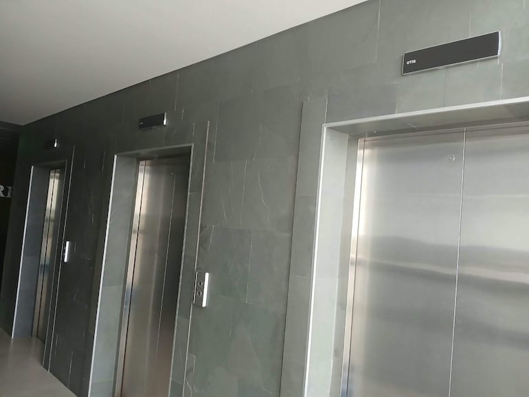 Vestíbulo con tres puertas de ascensor apagadas, acabado en piedra gris y ambiente moderno y vacío.