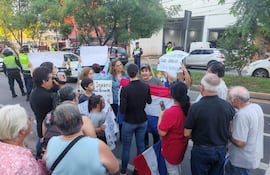 Mujer sostiene cartel en protesta, acompañada de otros vecinos, en un ambiente urbano con presencia policial.