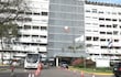 Edificio administrativo del IPS con autobús y automóvil estacionados, banderas y conos de tráfico visibles.