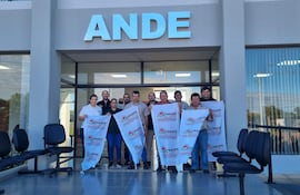 Grupo de trabajadores de la ANDE sosteniendo banderas de SITRANDE frente a un edificio, mostrando expresiones de unidad.